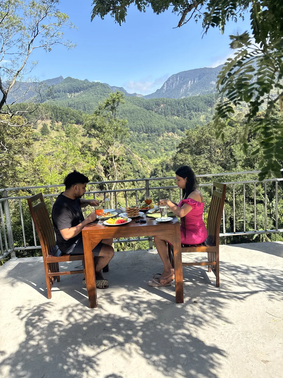Two guests at breakfast on the open deck, the valley and a rock face behind them