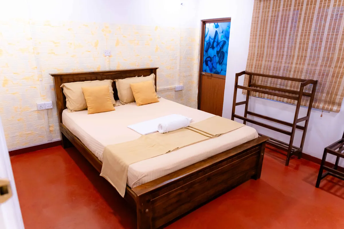 A double bed with mustard cushions, a wooden rack and chair, and a red floor