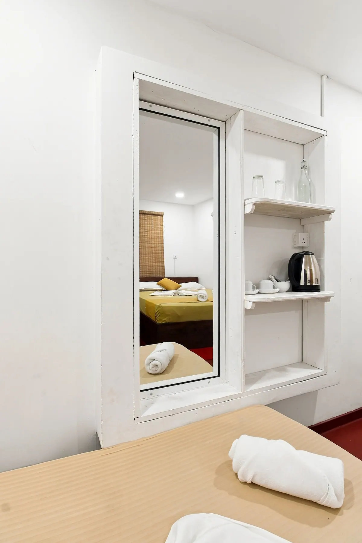 A mirror and shelves with a kettle and cups set into the wall of a bedroom