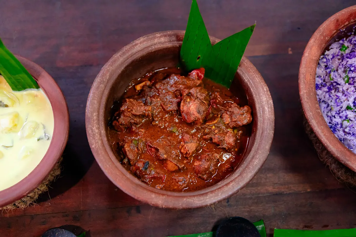 A dark meat curry in a clay pot, banana leaf tucked behind it