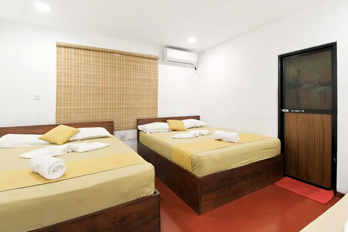 Two made-up beds with mustard throws and rolled towels in a white room with a terracotta floor