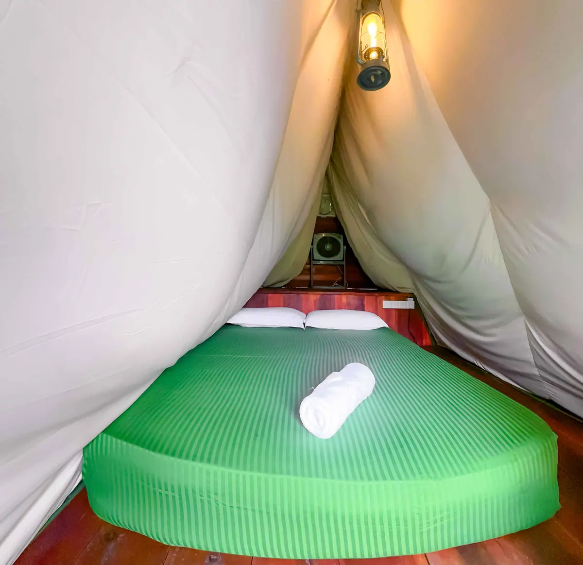 A bed made up with a rolled towel under cream canvas, lantern hanging at the peak