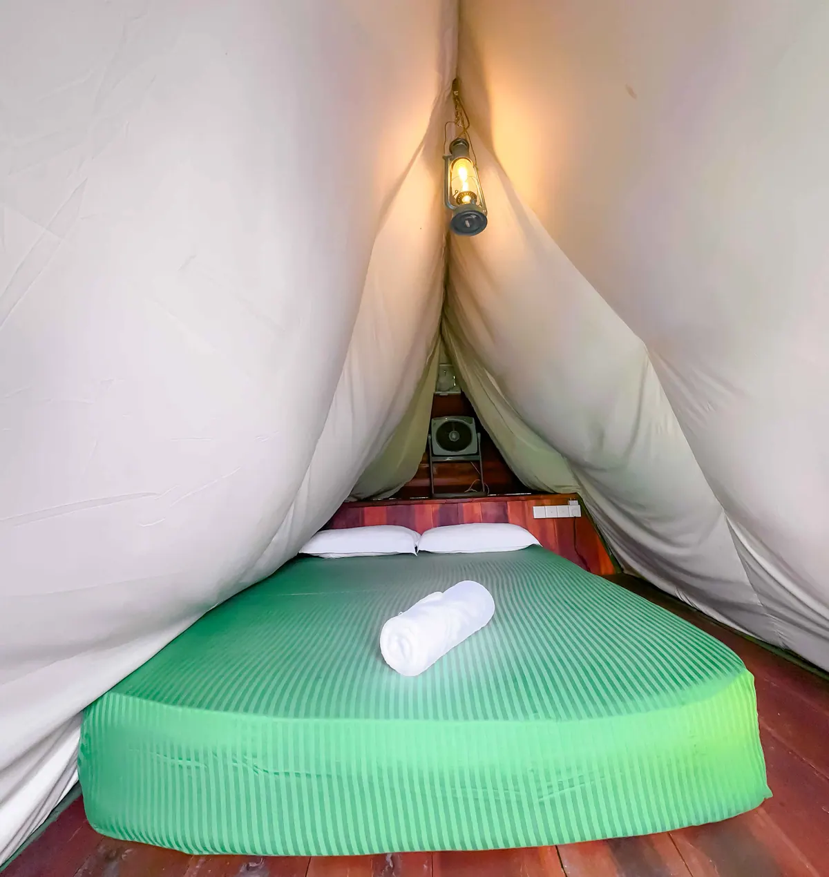Inside a cabin: a green-covered bed under draped canvas, a lantern lit above it