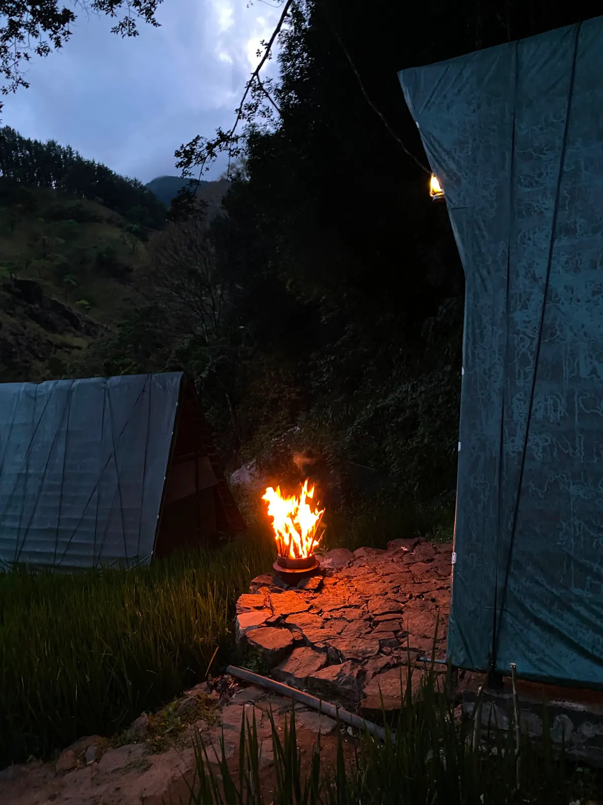 A fire burning between two cabins at dusk