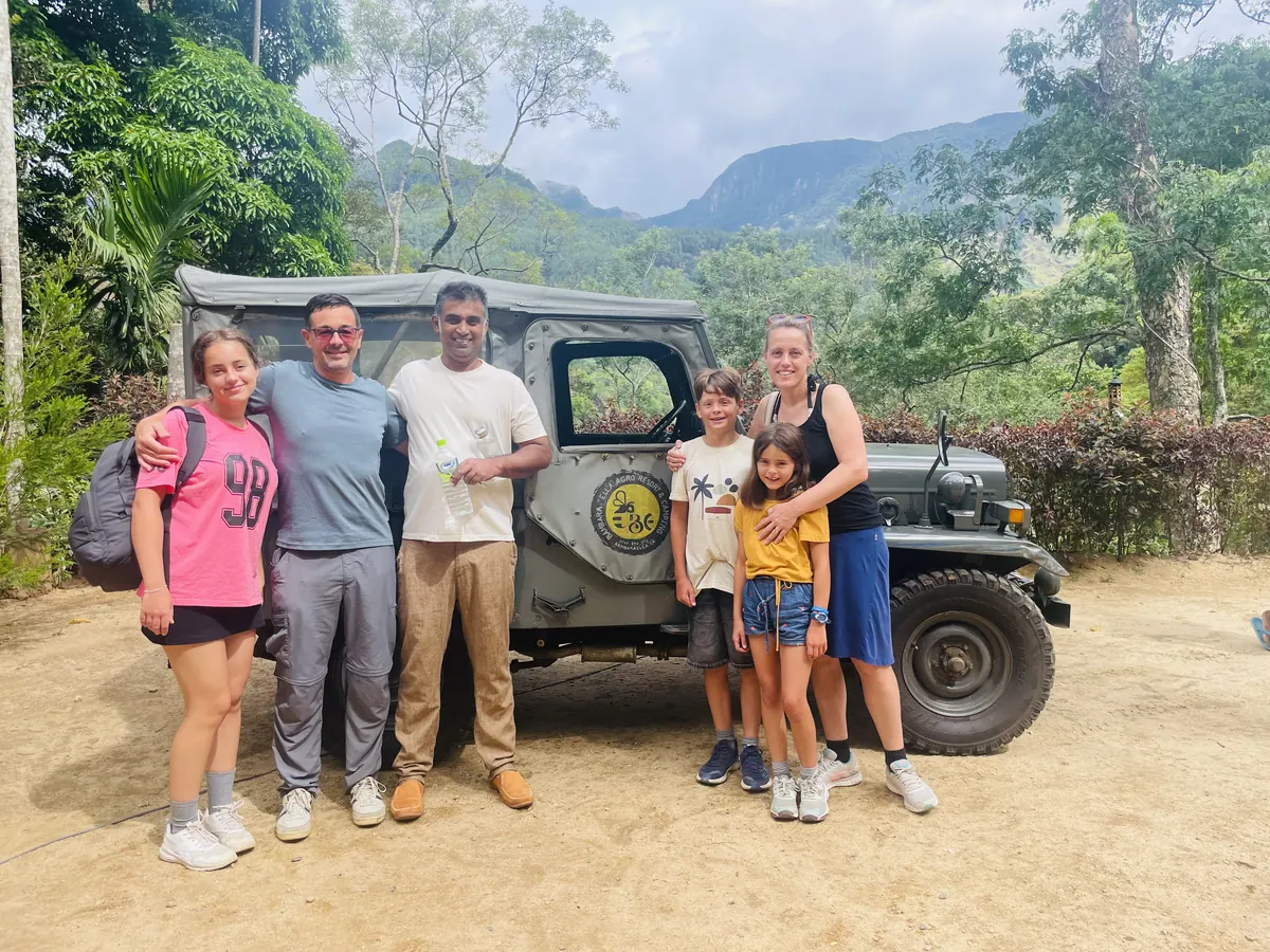 A family beside the Bambara Ella jeep on a dirt track, mountains behind