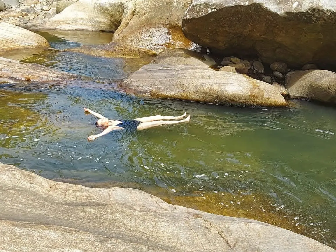 A swimmer floating in a clear rock pool between smooth boulders
