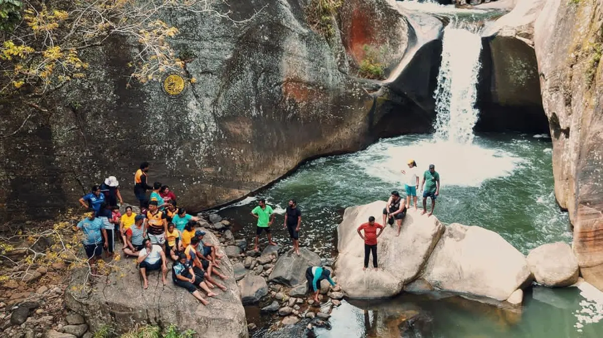The waterfall and its pool between smooth boulders, walkers on the rocks